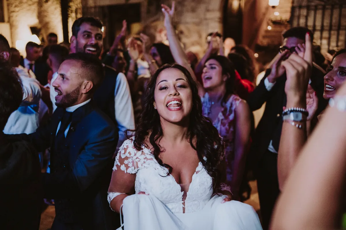 Bride laughing in the middle of a crowded dance floor with guests' arms in the air