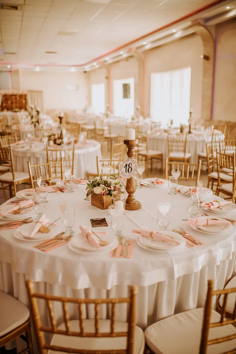 Round reception table with a numbered candle holder, pink napkins and gold chairs