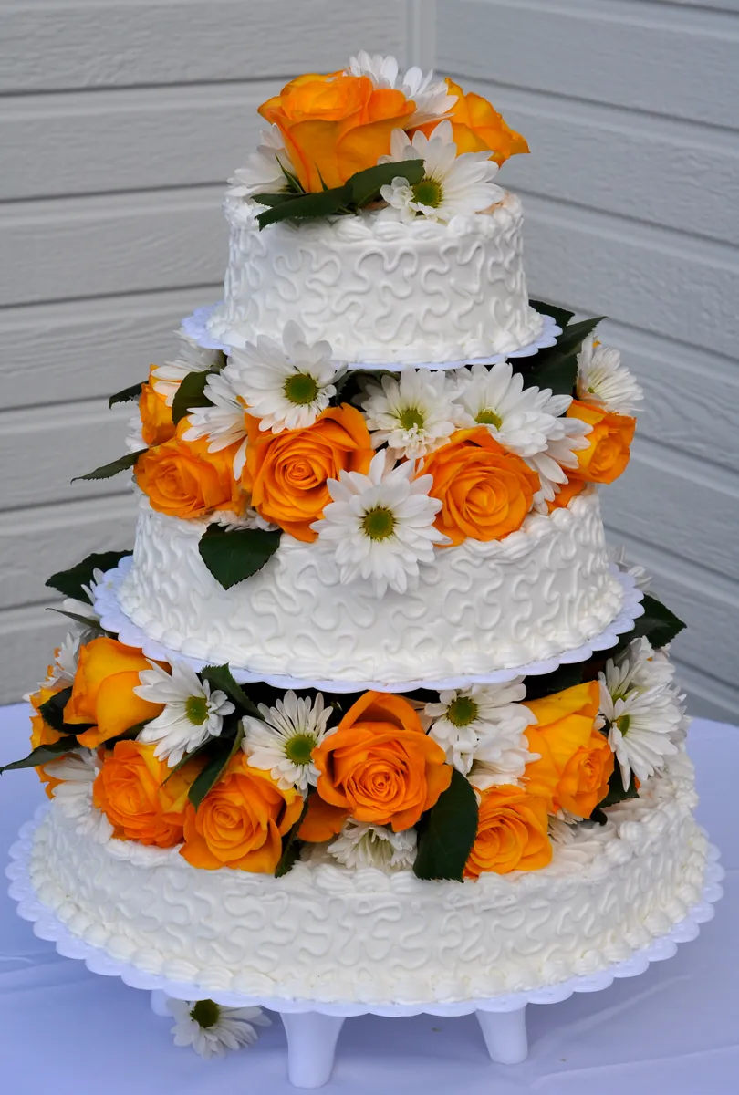 Three-tier white wedding cake decorated with orange roses and white daisies